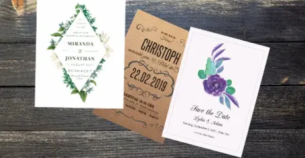 Drei Hochzeitseinladungen auf einem Holztisch.